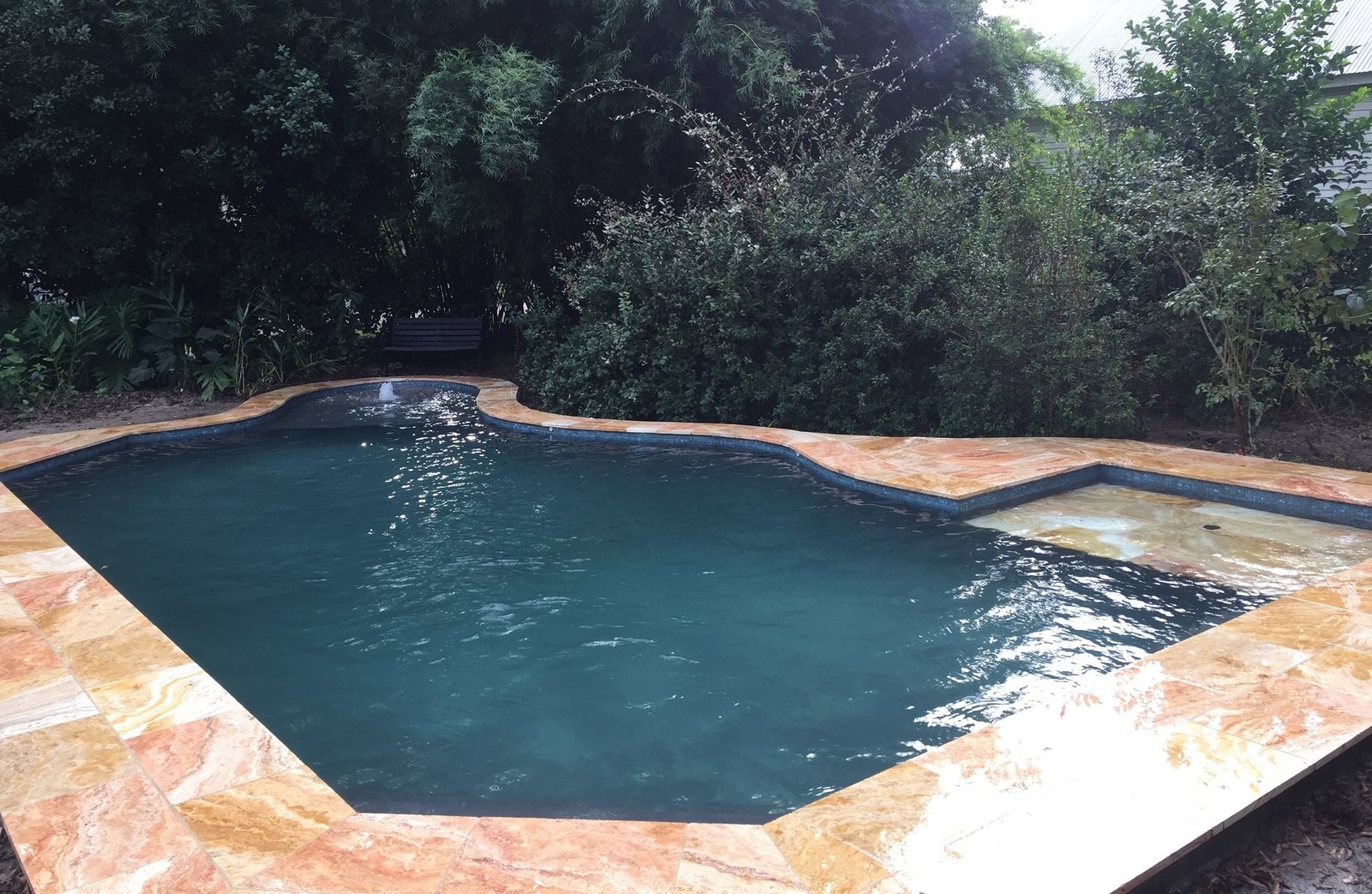 Free-form pool with dark water and a warm stone deck