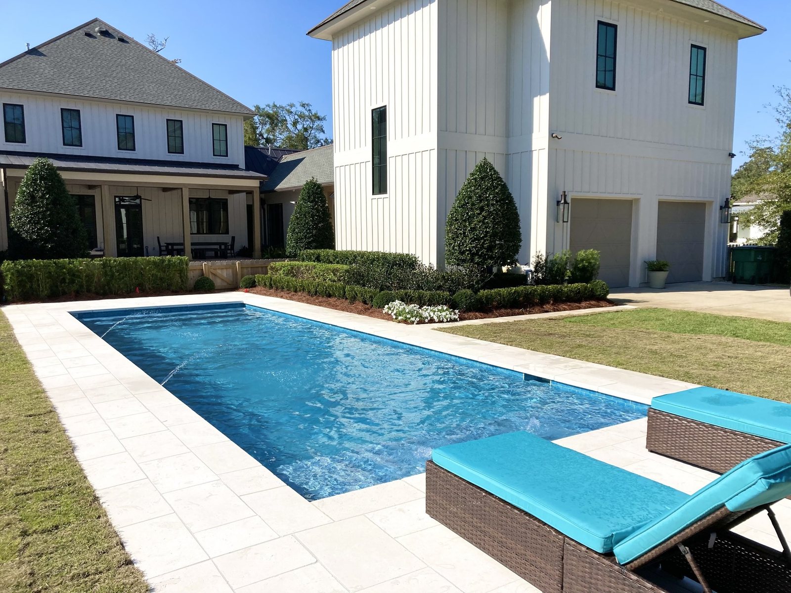 Geometric rectangular pool with stone deck and a white house beyond